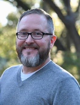 headshot of man with beard and glasses smiling