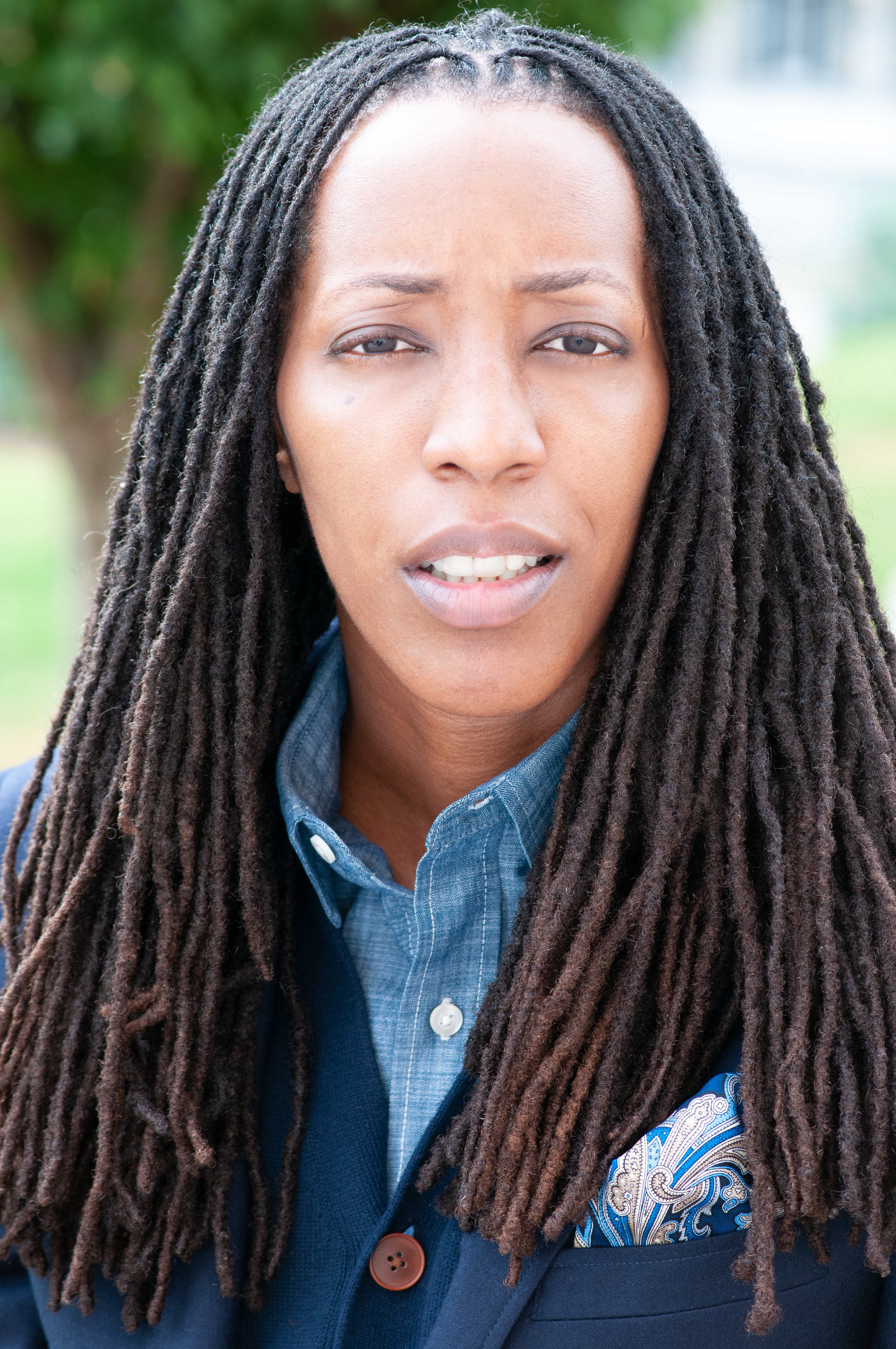 head and shoulders portrait photo of an African American woman with long locs looking intently into camera