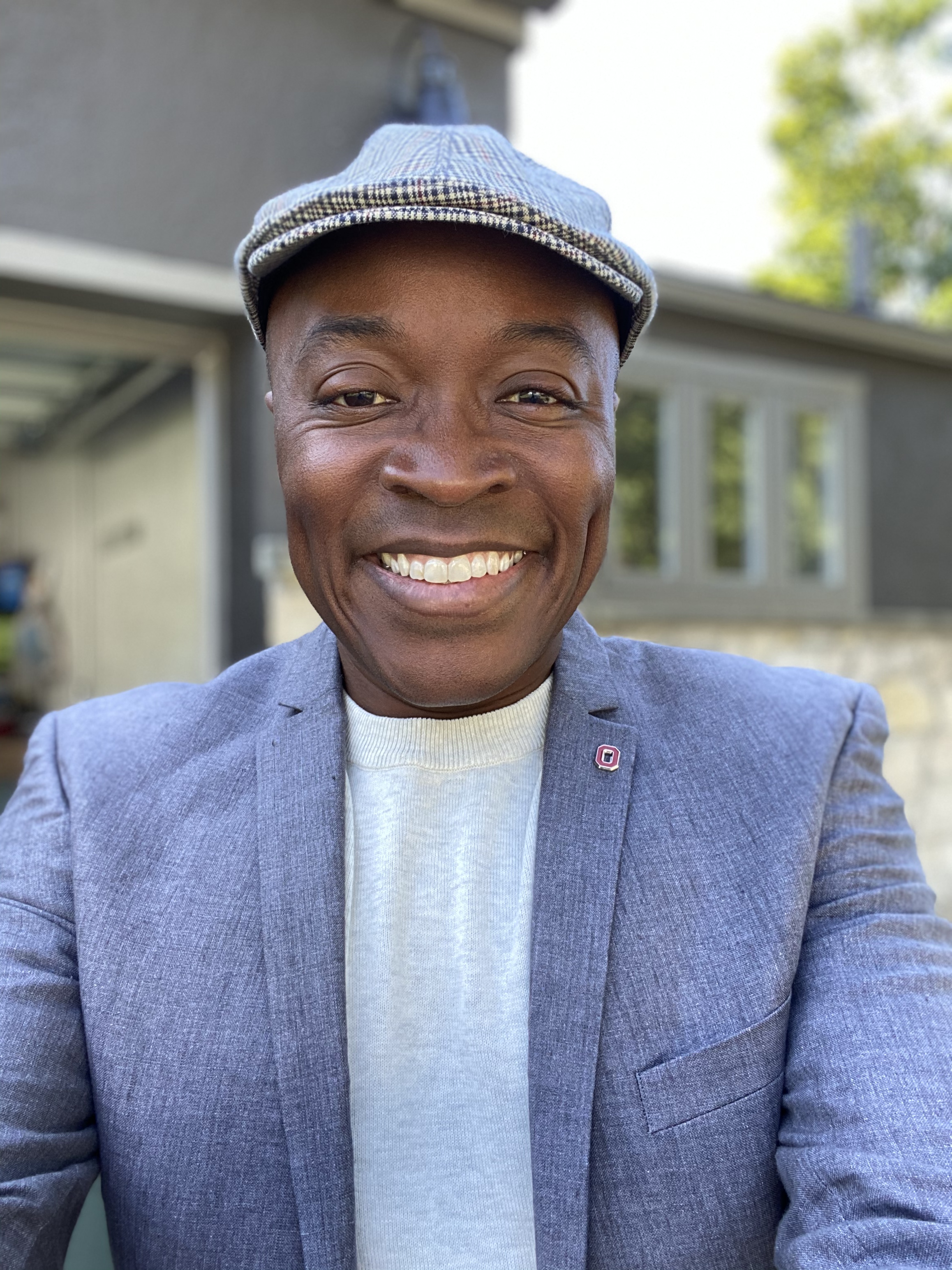 head and shoulders portrait photo of smiling African American man wearing a gray hat and blazer